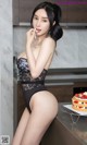 A woman in a black lingerie sitting on a counter next to a cake.