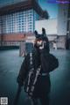 A woman wearing a black jacket and a cat mask.
