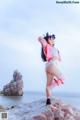 A woman in a bikini standing on a rock by the ocean.