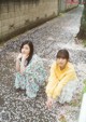 Two young women sitting on the ground in front of a tree.