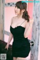 A woman in a black dress leaning against a door.