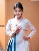 A woman in a white and blue hanbok poses for a picture.