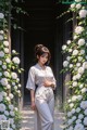 A woman standing in front of a wall of white roses.