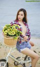 A woman sitting on a bike with a basket full of flowers.