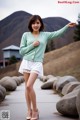 A woman in a green cardigan and white skirt posing for a picture.