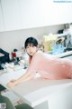 A woman in a pink dress sitting at a kitchen counter.