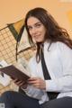 A woman in a white shirt and tie is reading a book.