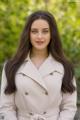 A woman in a beige trench coat posing for a picture.