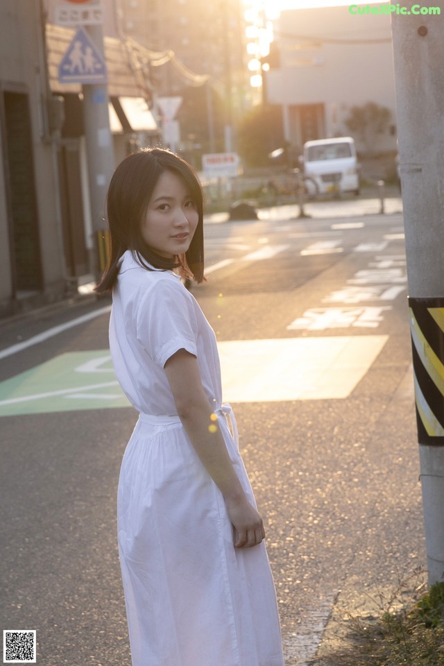 A woman in a white dress standing on the side of a road.