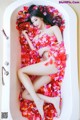 A woman laying in a bathtub covered in rose petals.