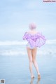 A woman in a purple and white plaid shirt is walking on the beach.